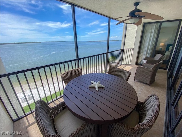 sunroom / solarium with ceiling fan, a water view, a healthy amount of sunlight, and a view of the beach