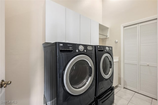 laundry area featuring washer and dryer, light tile patterned floors, and cabinets