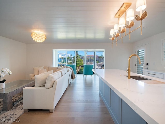 kitchen featuring light stone countertops, sink, light hardwood / wood-style flooring, a notable chandelier, and decorative light fixtures