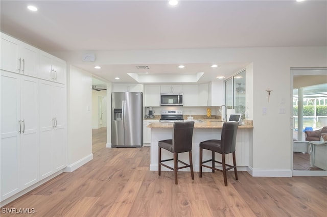 kitchen featuring white cabinets, a kitchen breakfast bar, stainless steel appliances, and kitchen peninsula