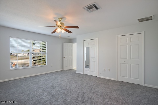 unfurnished bedroom with ceiling fan, dark carpet, and multiple closets