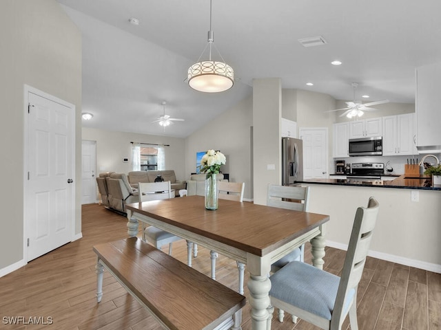 dining space featuring ceiling fan, wood-type flooring, sink, and high vaulted ceiling