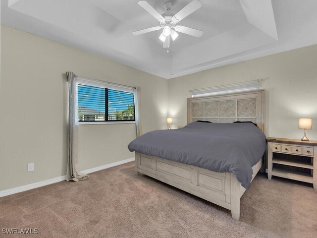 carpeted bedroom with a raised ceiling and ceiling fan