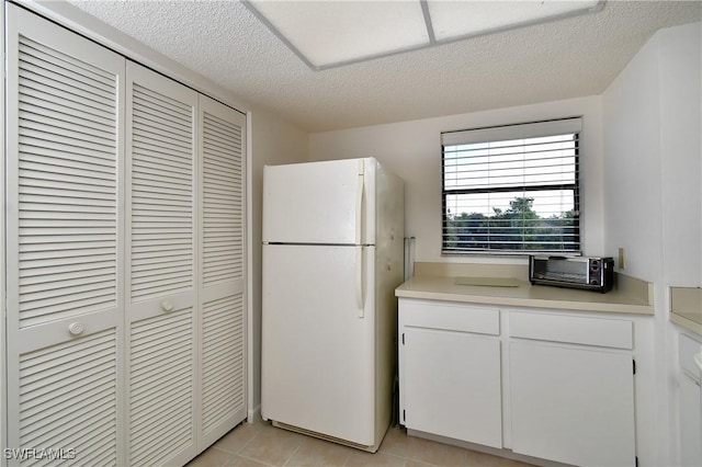 kitchen with white cabinets, white refrigerator, light tile patterned floors, and a textured ceiling