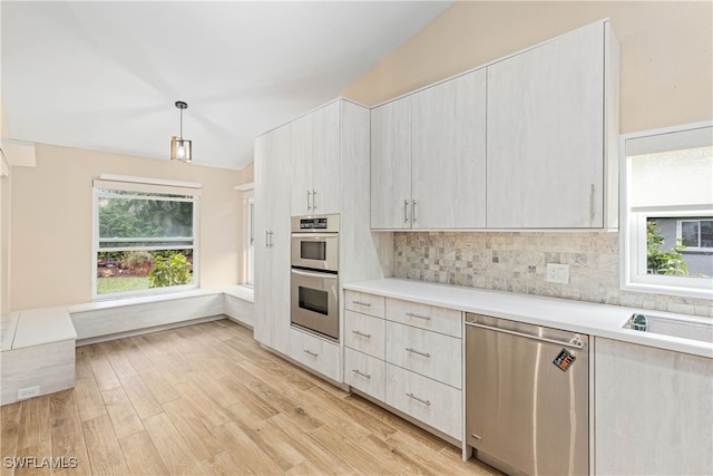 kitchen with light hardwood / wood-style floors, pendant lighting, vaulted ceiling, decorative backsplash, and appliances with stainless steel finishes