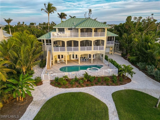 rear view of property with outdoor lounge area, a swimming pool with hot tub, a balcony, a yard, and a patio area