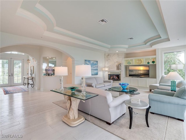 living room featuring arched walkways, ornamental molding, visible vents, a raised ceiling, and french doors