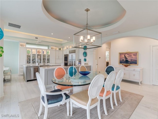 dining area featuring light hardwood / wood-style floors, sink, a raised ceiling, and a chandelier