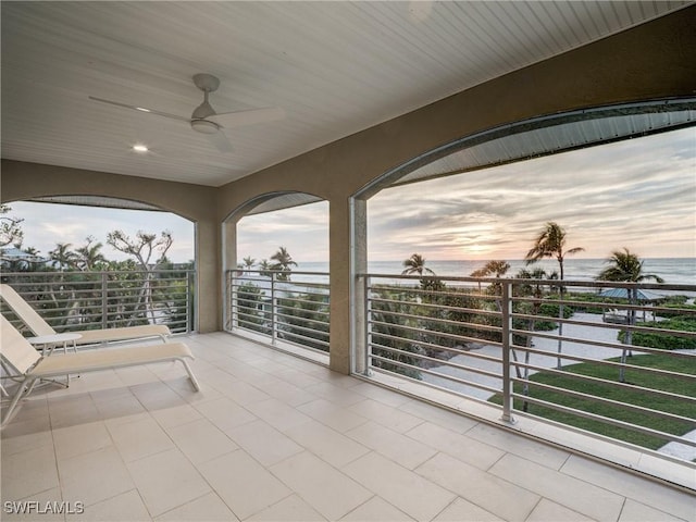 patio terrace at dusk featuring a water view, ceiling fan, and a balcony