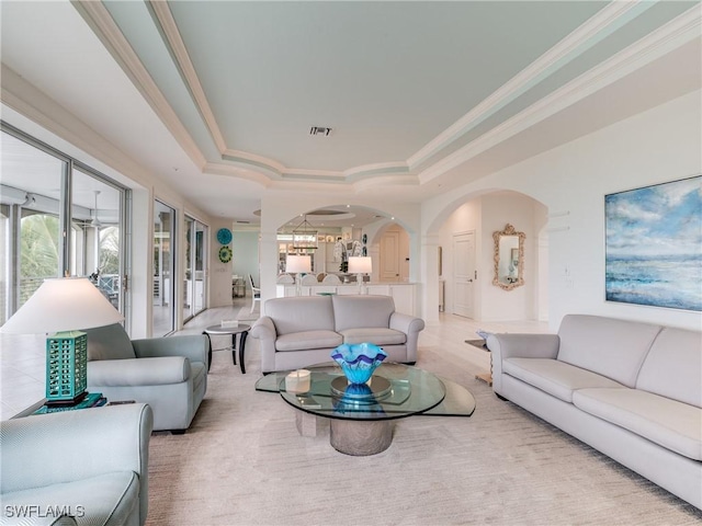 living room featuring ornamental molding, arched walkways, visible vents, and a tray ceiling