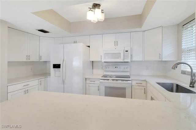 kitchen featuring a raised ceiling, white cabinetry, sink, and white appliances