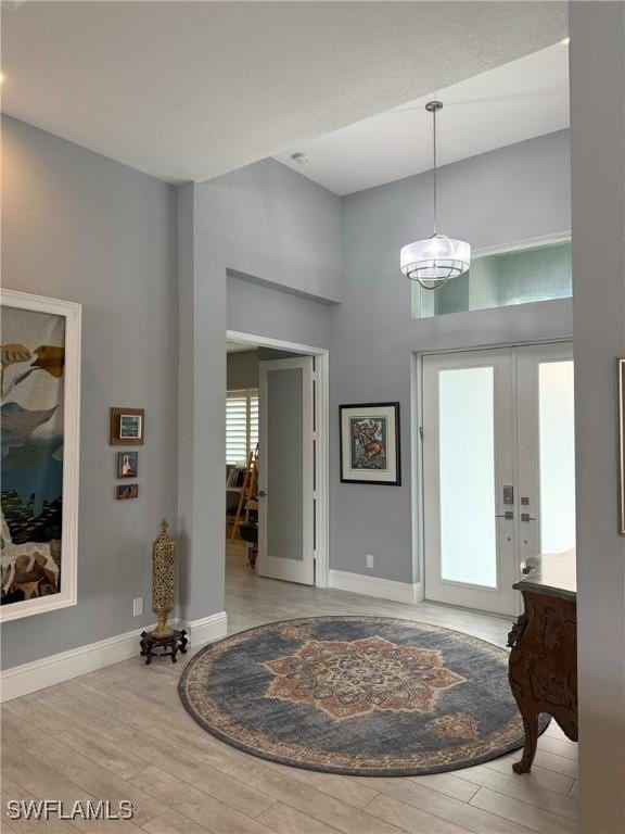 entrance foyer with french doors, a towering ceiling, and light hardwood / wood-style floors