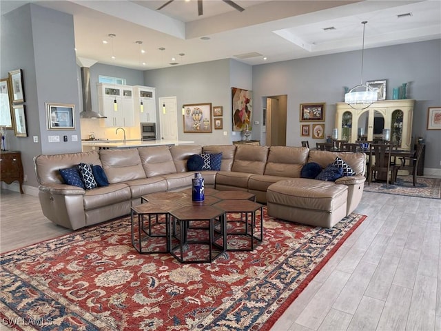 living room featuring a high ceiling, a raised ceiling, sink, light hardwood / wood-style floors, and a chandelier