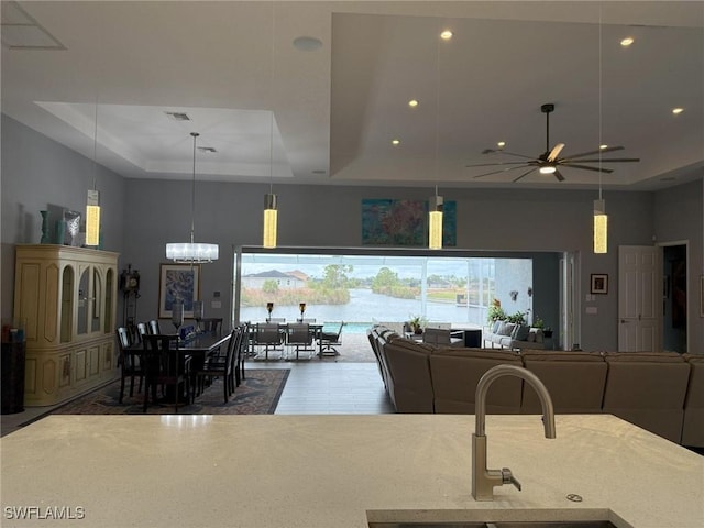 kitchen featuring pendant lighting, ceiling fan with notable chandelier, sink, and a tray ceiling