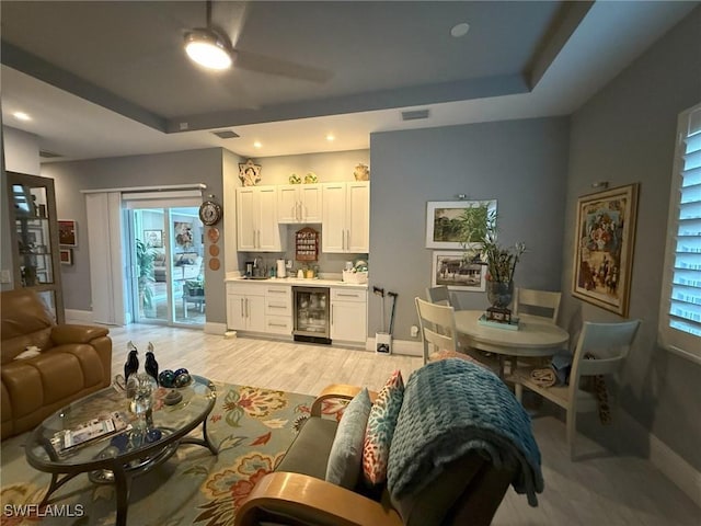 living room with a raised ceiling, light wood-type flooring, and beverage cooler