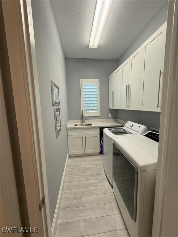 laundry area with cabinets, a textured ceiling, sink, washing machine and clothes dryer, and light hardwood / wood-style floors