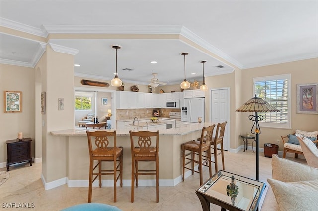 kitchen featuring a breakfast bar, white appliances, decorative light fixtures, light stone counters, and white cabinetry