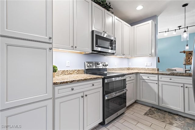 kitchen featuring light stone countertops, rail lighting, stainless steel appliances, decorative light fixtures, and white cabinetry