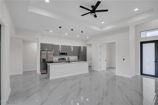 kitchen with a kitchen island with sink, a raised ceiling, hanging light fixtures, ceiling fan, and stainless steel appliances