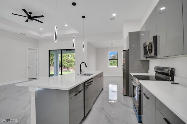 kitchen with sink, stainless steel appliances, decorative light fixtures, gray cabinets, and a kitchen island with sink