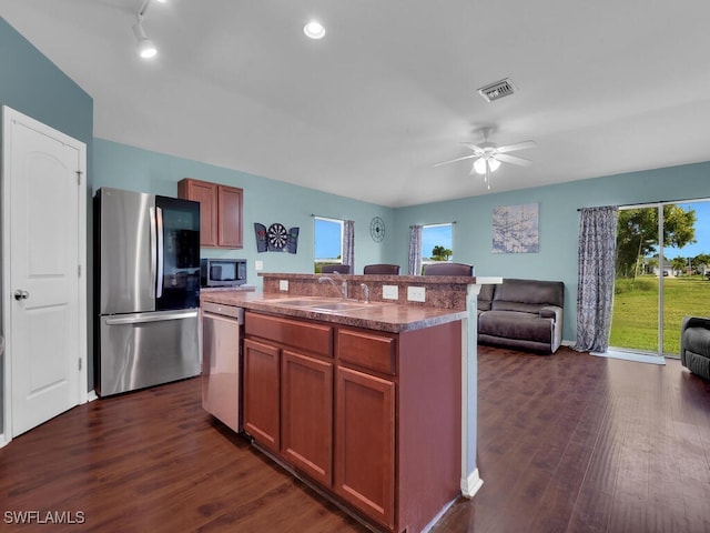 kitchen with appliances with stainless steel finishes, ceiling fan, sink, a center island with sink, and dark hardwood / wood-style floors