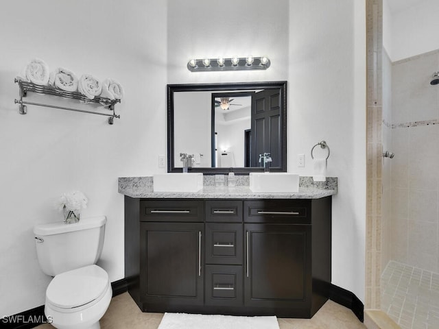 bathroom with vanity, a tile shower, toilet, and baseboards