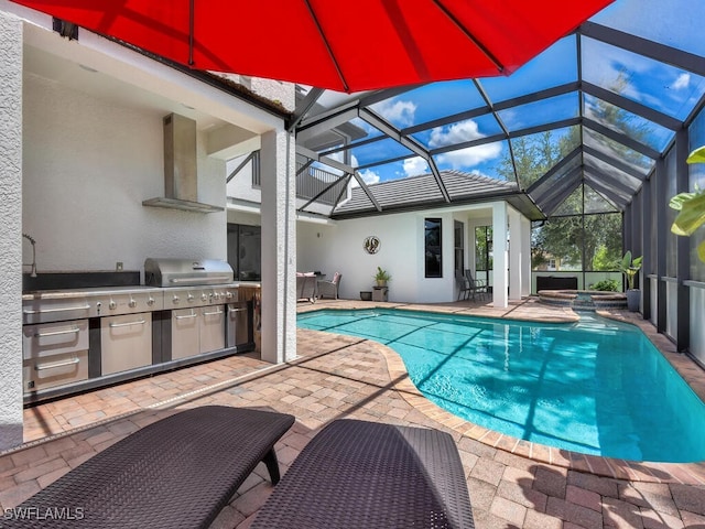 view of pool with exterior kitchen, glass enclosure, a pool with connected hot tub, and a patio area