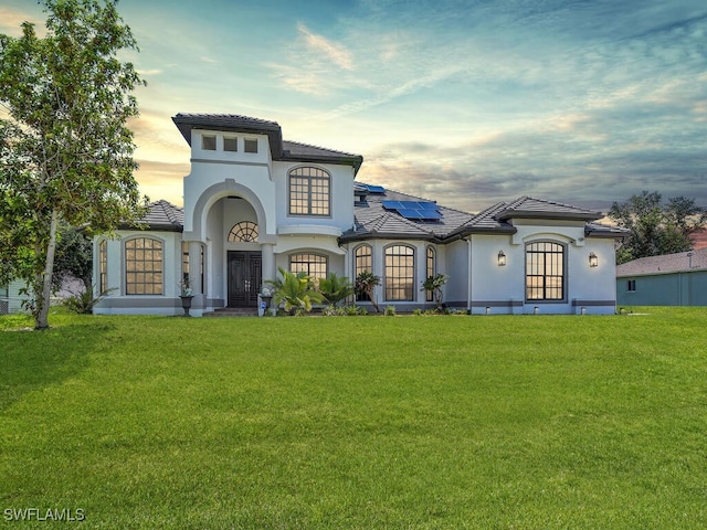 mediterranean / spanish home featuring a lawn and solar panels