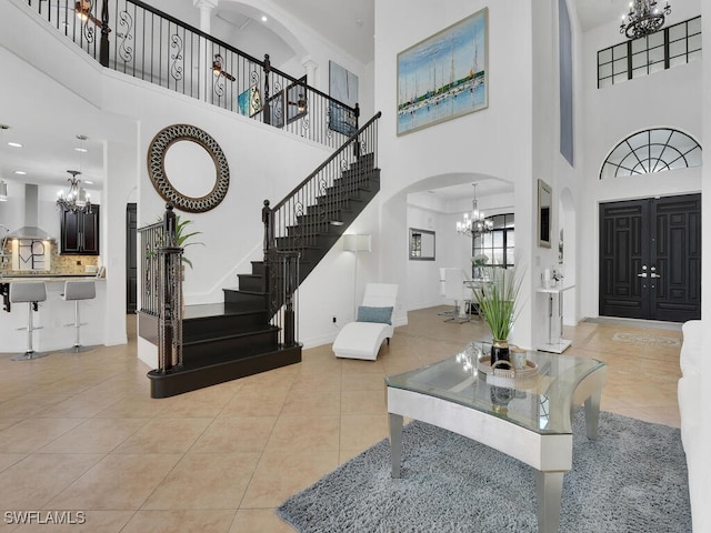 entrance foyer featuring arched walkways, light tile patterned floors, an inviting chandelier, baseboards, and stairs