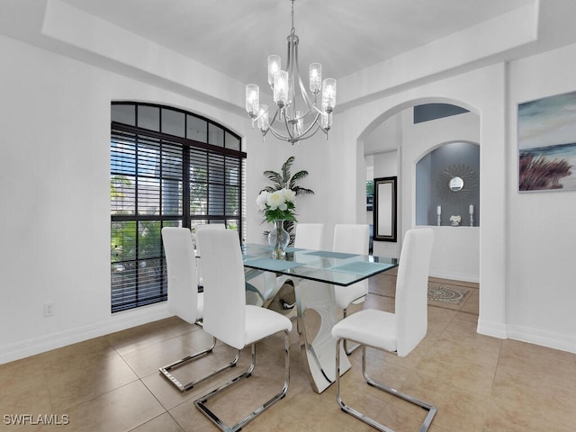 tiled dining space featuring baseboards, a raised ceiling, and a notable chandelier