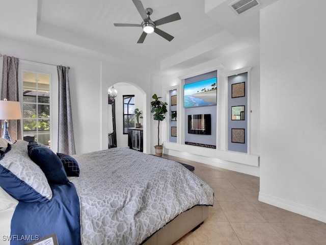 bedroom featuring light tile patterned floors, baseboards, visible vents, arched walkways, and a tray ceiling