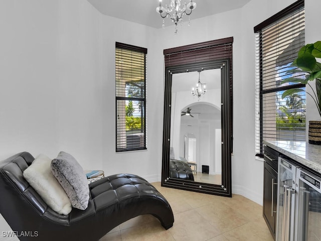 sitting room featuring arched walkways, light tile patterned floors, beverage cooler, baseboards, and ceiling fan with notable chandelier