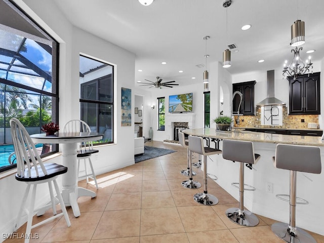 kitchen with light tile patterned floors, light stone countertops, decorative backsplash, wall chimney exhaust hood, and a kitchen bar