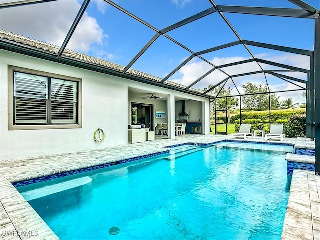 view of pool featuring glass enclosure, ceiling fan, an outdoor kitchen, and a patio area