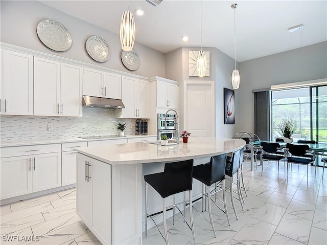 kitchen featuring white cabinets, hanging light fixtures, and a center island with sink