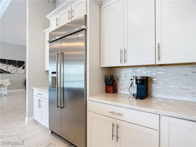 kitchen featuring white cabinets, decorative backsplash, built in fridge, and light stone counters