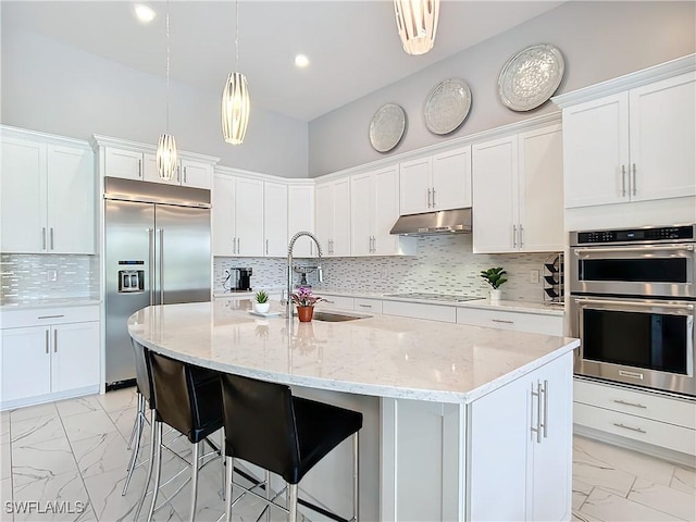 kitchen featuring appliances with stainless steel finishes, white cabinets, sink, pendant lighting, and a center island with sink