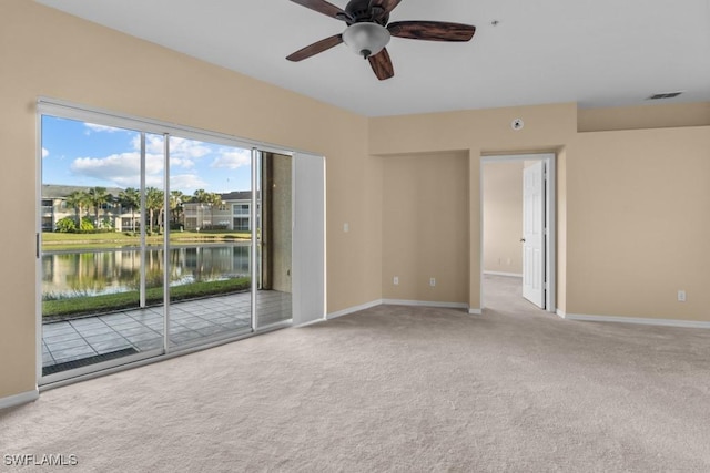 spare room with ceiling fan, a water view, and light carpet