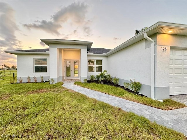 exterior entry at dusk featuring french doors, a yard, and a garage