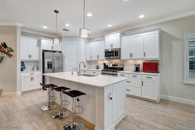 kitchen with sink, hanging light fixtures, stainless steel appliances, white cabinets, and a center island with sink