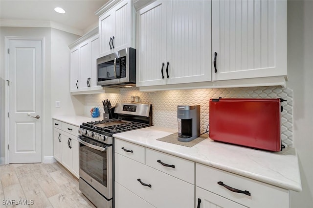 kitchen featuring white cabinets, backsplash, ornamental molding, stainless steel appliances, and light hardwood / wood-style flooring