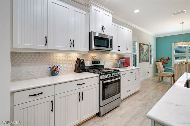 kitchen featuring pendant lighting, backsplash, stainless steel appliances, ornamental molding, and white cabinets