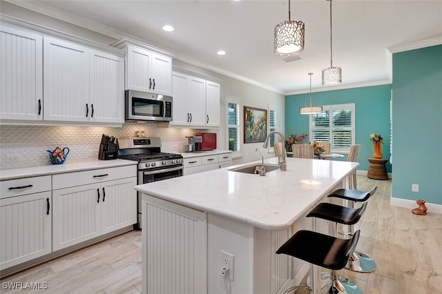 kitchen with sink, white cabinetry, decorative light fixtures, appliances with stainless steel finishes, and a kitchen island with sink