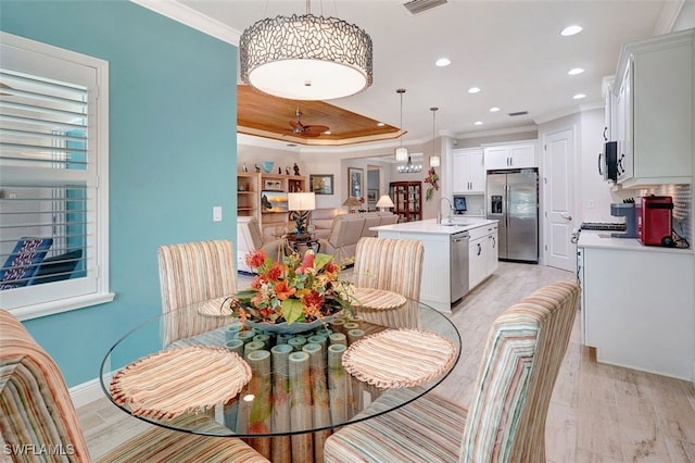 dining room with ornamental molding, a tray ceiling, sink, and light wood-type flooring