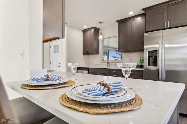 kitchen featuring stainless steel appliances, light stone counters, hanging light fixtures, and sink