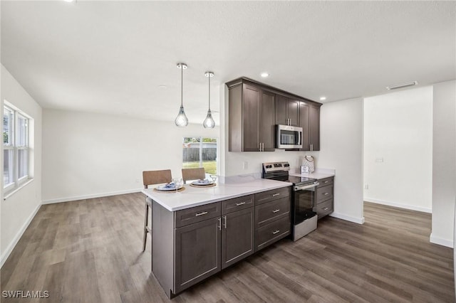 kitchen featuring decorative light fixtures, dark hardwood / wood-style flooring, stainless steel appliances, and a breakfast bar area