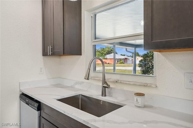 kitchen with dark brown cabinetry, dishwasher, sink, and light stone countertops