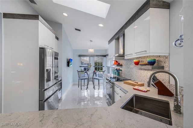 kitchen featuring appliances with stainless steel finishes, backsplash, wall chimney range hood, sink, and white cabinets