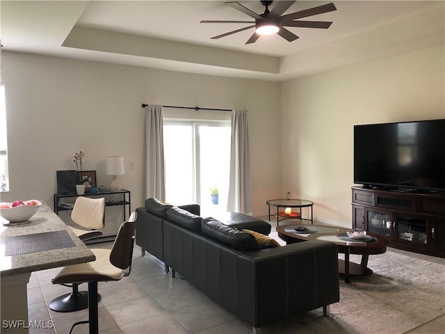 living room featuring light tile patterned floors, ceiling fan, and a tray ceiling