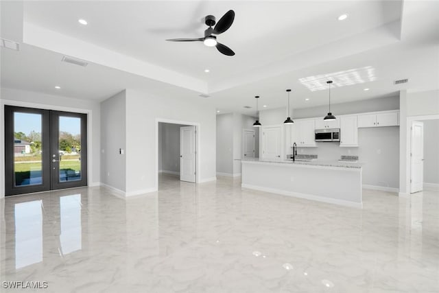 unfurnished living room featuring ceiling fan, sink, a tray ceiling, and french doors